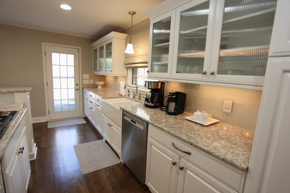 Example of a mid-sized classic galley medium tone wood floor and brown floor eat-in kitchen design in Indianapolis with a farmhouse sink, raised-panel cabinets, white cabinets, granite countertops, beige backsplash, glass tile backsplash, stainless steel appliances and a peninsula