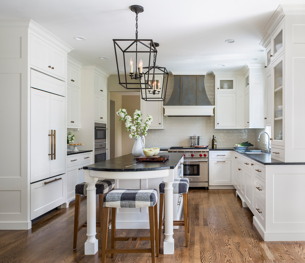 Mid-sized elegant medium tone wood floor and brown floor kitchen photo in Minneapolis with a single-bowl sink, recessed-panel cabinets, white cabinets, granite countertops, white backsplash, ceramic backsplash, stainless steel appliances, an island and black countertops