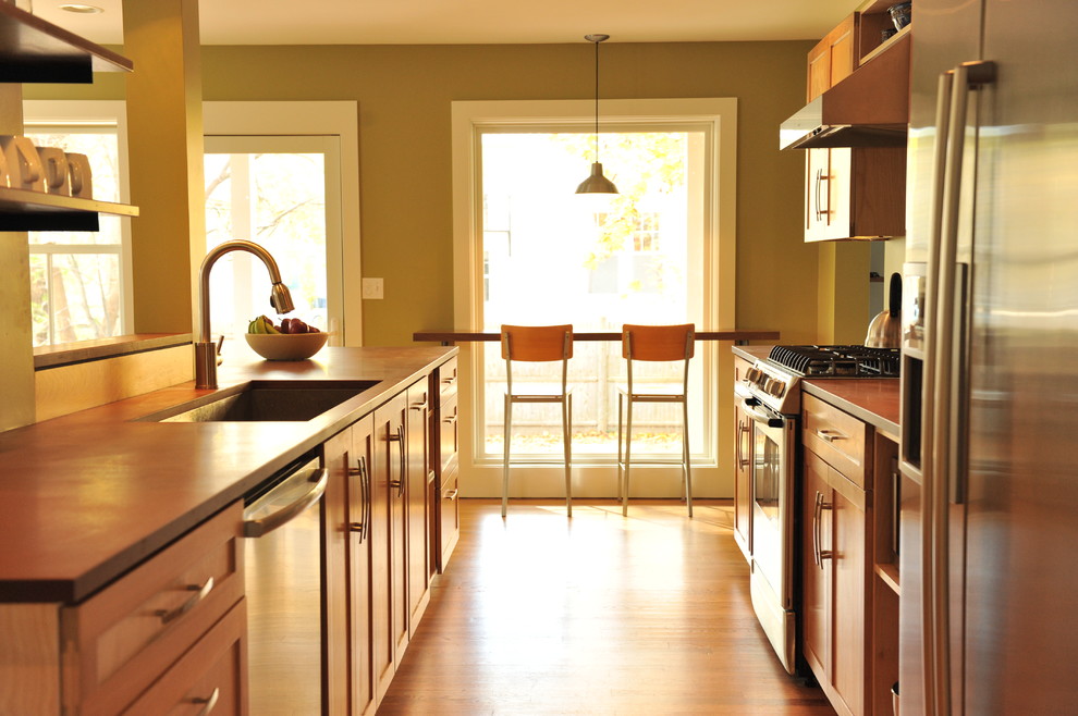Foto på ett funkis kök, med en undermonterad diskho, luckor med infälld panel, skåp i mellenmörkt trä, rostfria vitvaror, mellanmörkt trägolv och en köksö