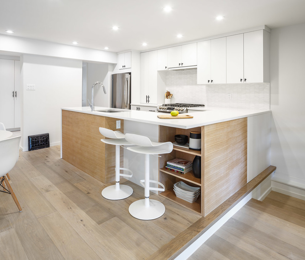 Modern inredning av ett litet kök, med en undermonterad diskho, släta luckor, vita skåp, bänkskiva i kvarts, vitt stänkskydd, stänkskydd i stenkakel, rostfria vitvaror, ljust trägolv, en halv köksö och beiget golv