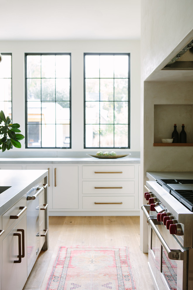 Imagen de cocina costera grande con armarios con paneles lisos, puertas de armario blancas, encimera de cemento, salpicadero blanco y una isla