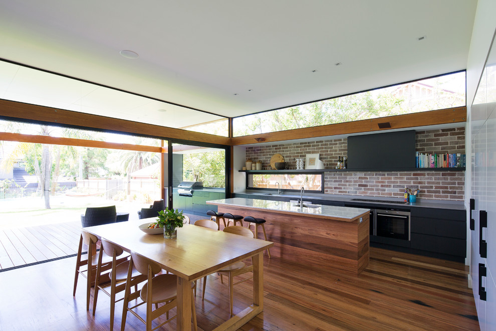 Cette photo montre une grande cuisine ouverte parallèle tendance avec un évier encastré, plan de travail en marbre, un électroménager en acier inoxydable, un sol en bois brun et îlot.