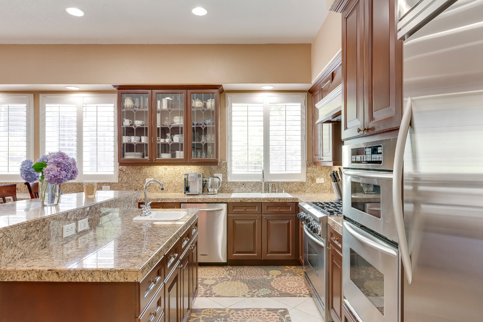 Example of a huge classic u-shaped ceramic tile eat-in kitchen design in Sacramento with a double-bowl sink, glass-front cabinets, medium tone wood cabinets, granite countertops, brown backsplash, stone tile backsplash, stainless steel appliances and a peninsula