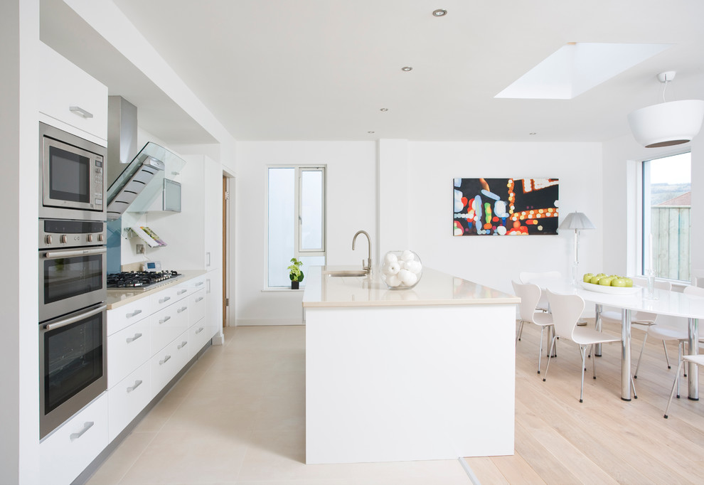 Inspiration for a large contemporary u-shaped light wood floor eat-in kitchen remodel in Dublin with an undermount sink, flat-panel cabinets, white cabinets, white backsplash, stainless steel appliances and an island