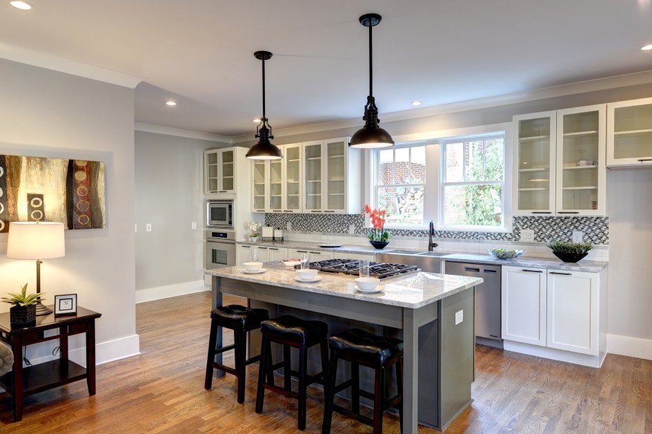 Example of a mid-sized eclectic galley medium tone wood floor eat-in kitchen design in Atlanta with a farmhouse sink, shaker cabinets, white cabinets, granite countertops, multicolored backsplash, stone tile backsplash, stainless steel appliances and an island