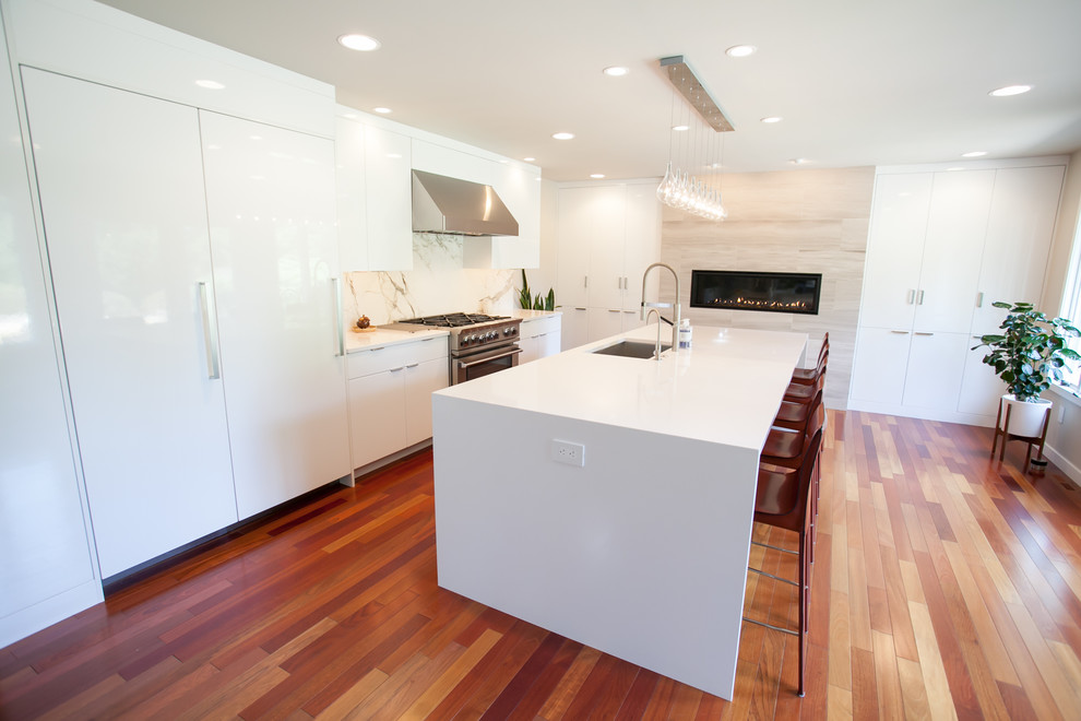 Large trendy galley medium tone wood floor and brown floor open concept kitchen photo in Philadelphia with an undermount sink, flat-panel cabinets, white cabinets, quartz countertops, white backsplash, stone slab backsplash, paneled appliances and an island