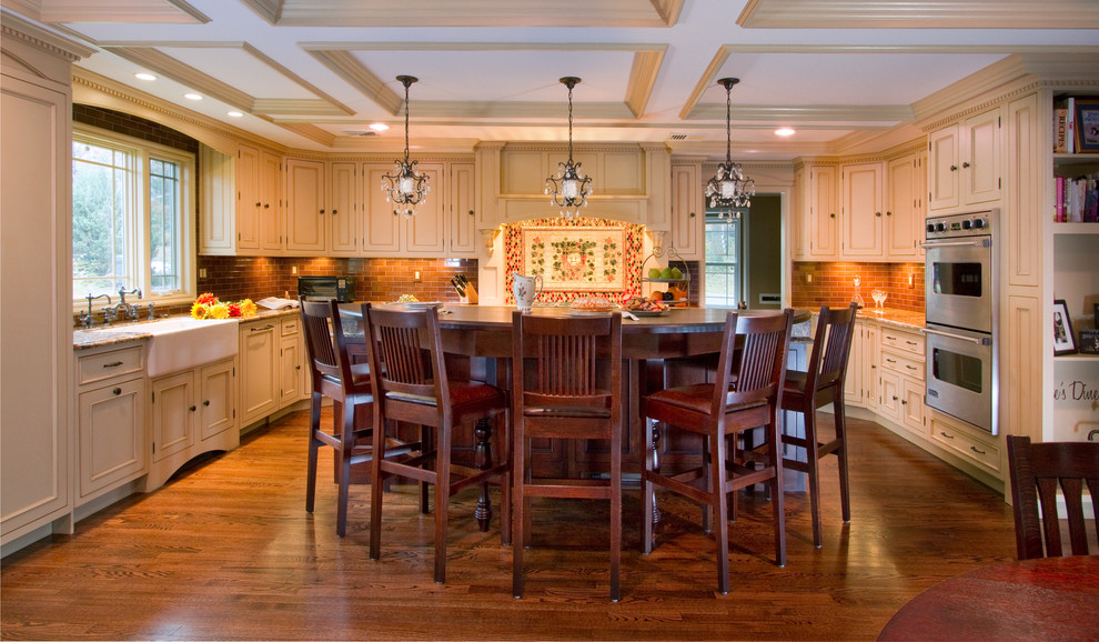 Klassisk inredning av ett stort flerfärgad flerfärgat kök, med en rustik diskho, luckor med profilerade fronter, beige skåp, granitbänkskiva, rött stänkskydd, stänkskydd i tunnelbanekakel, integrerade vitvaror, mellanmörkt trägolv, en köksö och brunt golv