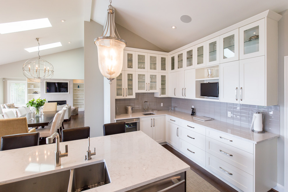 Example of a large transitional l-shaped medium tone wood floor eat-in kitchen design in Vancouver with an undermount sink, shaker cabinets, white cabinets, quartzite countertops, glass tile backsplash, stainless steel appliances, an island, white backsplash and white countertops