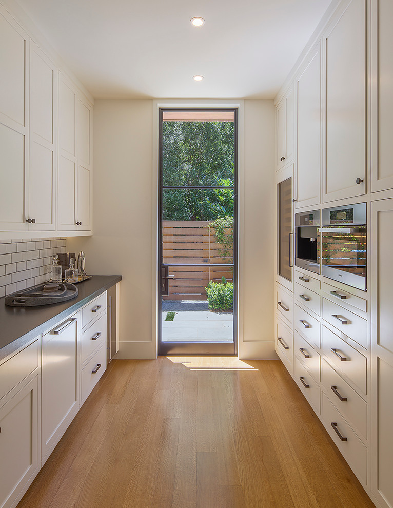 Kitchen - transitional galley medium tone wood floor kitchen idea in San Francisco with recessed-panel cabinets, beige cabinets, white backsplash, subway tile backsplash, stainless steel appliances and no island