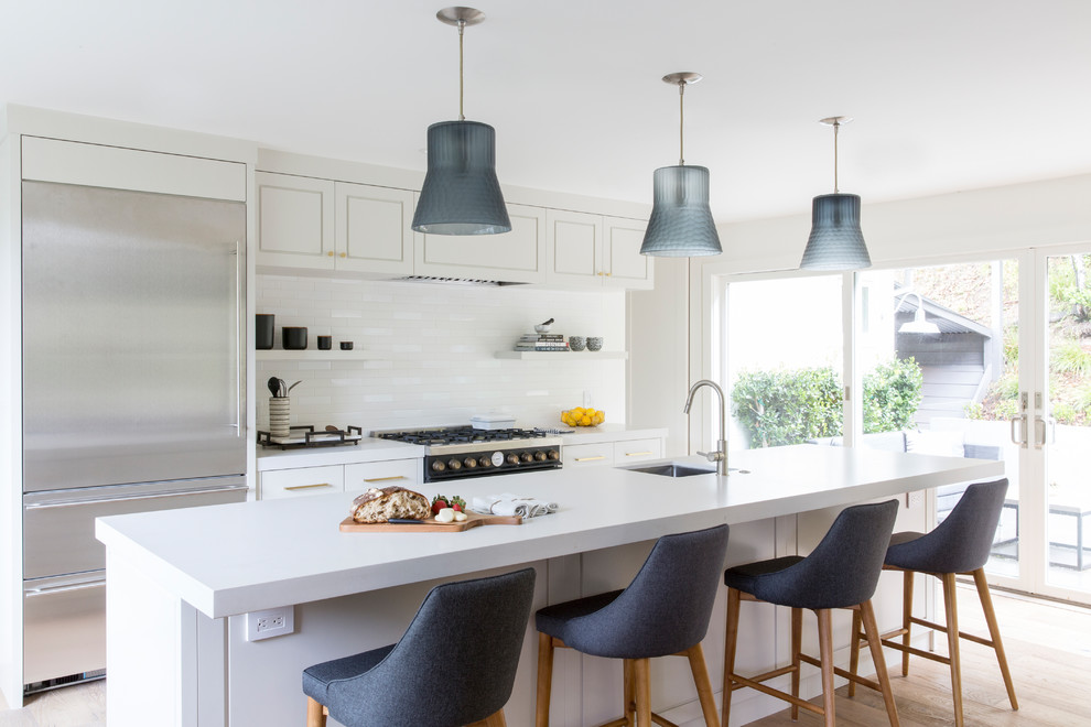 This is an example of a farmhouse kitchen in San Francisco with a single-bowl sink, flat-panel cabinets, grey cabinets, engineered stone countertops, white splashback, ceramic splashback, black appliances, light hardwood flooring, an island, brown floors and grey worktops.