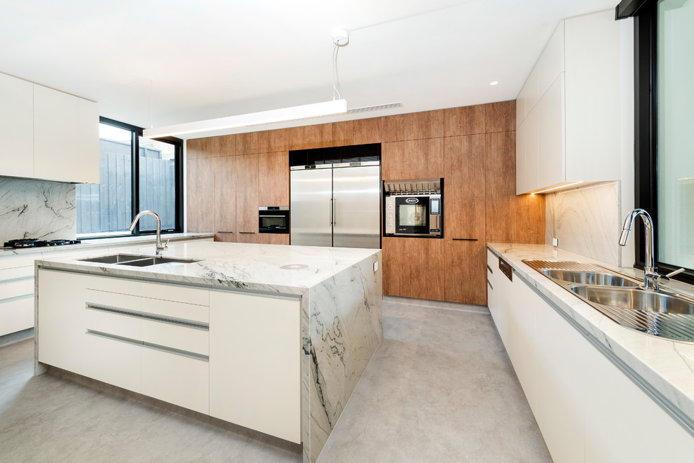 Moderne Küche in U-Form mit Einbauwaschbecken, flächenbündigen Schrankfronten, hellbraunen Holzschränken, Küchengeräten aus Edelstahl, Kücheninsel, grauem Boden und grauer Arbeitsplatte in Melbourne