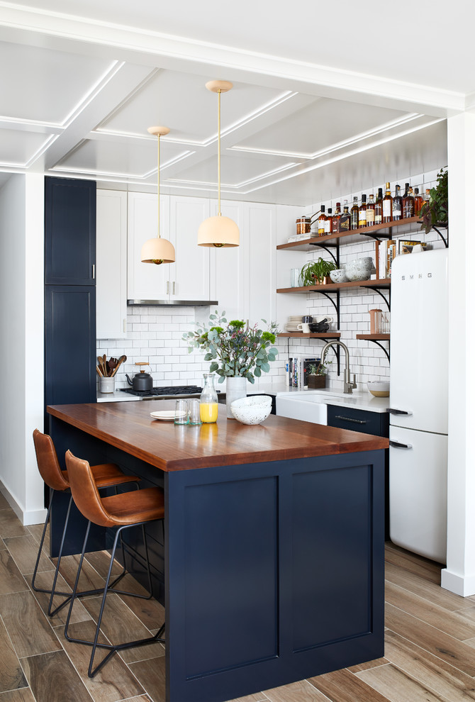 Example of a small eclectic l-shaped porcelain tile and brown floor open concept kitchen design in DC Metro with a farmhouse sink, shaker cabinets, blue cabinets, quartz countertops, white backsplash, ceramic backsplash, white appliances and an island
