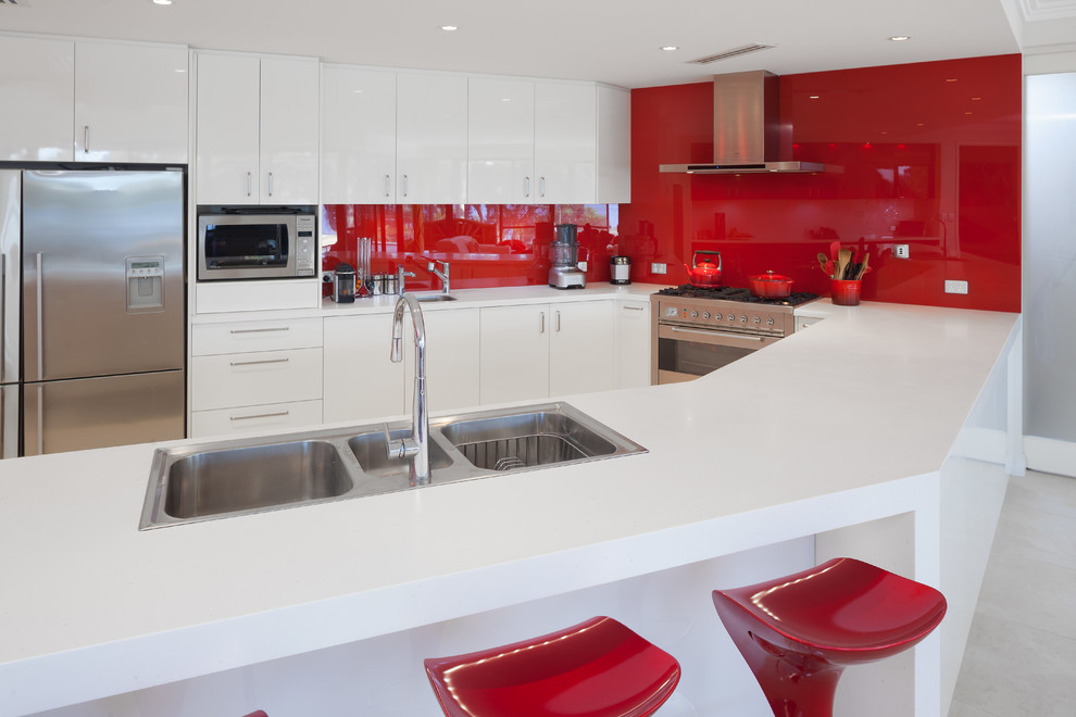 Inspiration for a contemporary kitchen remodel in Perth with a double-bowl sink, flat-panel cabinets, white cabinets, solid surface countertops, red backsplash, glass sheet backsplash, stainless steel appliances and white countertops