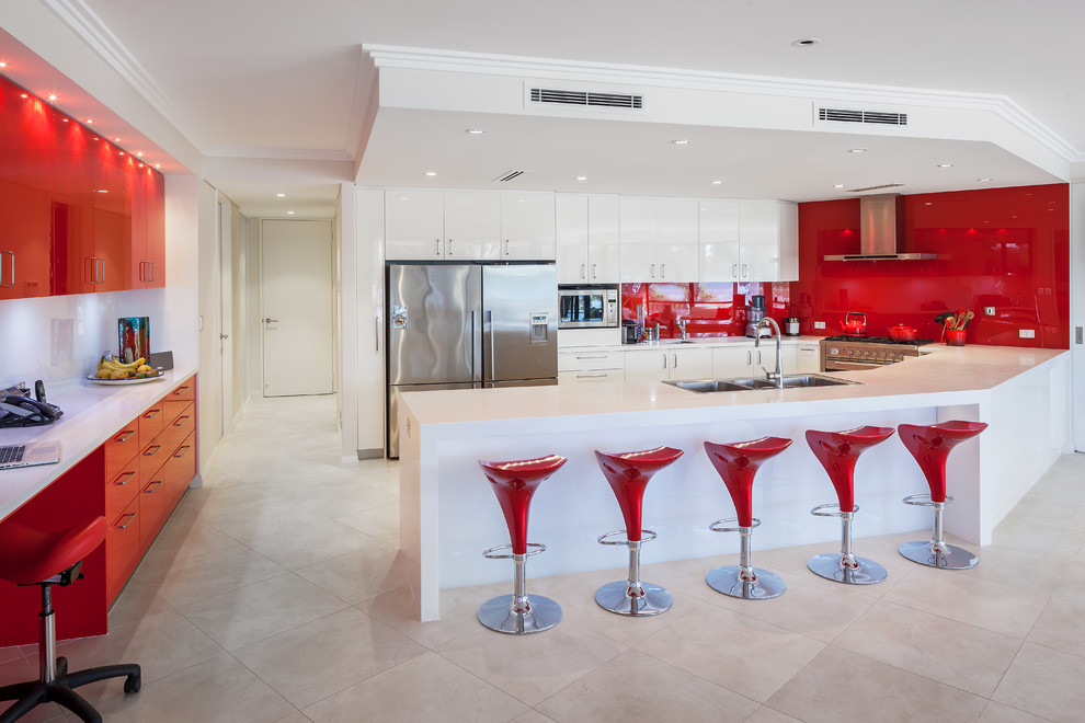 Immagine di una cucina contemporanea con ante lisce, ante bianche, top in superficie solida, paraspruzzi rosso, paraspruzzi con lastra di vetro, elettrodomestici in acciaio inossidabile e top bianco