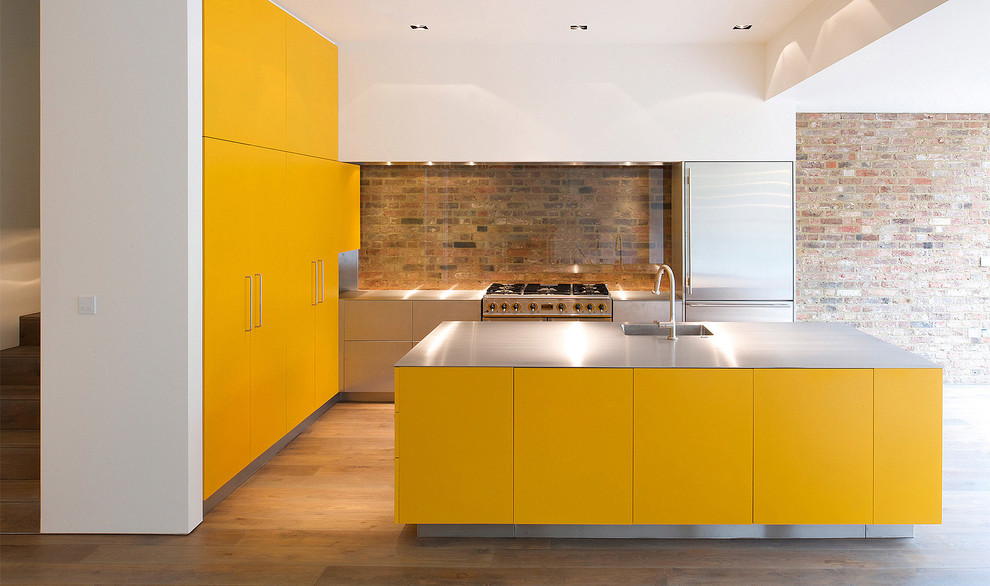 ロンドンにある高級な広いインダストリアルスタイルのおしゃれなキッチン (一体型シンク、フラットパネル扉のキャビネット、黄色いキャビネット、ステンレスカウンター、マルチカラーのキッチンパネル、ガラスタイルのキッチンパネル、シルバーの調理設備、ラミネートの床、茶色い床) の写真