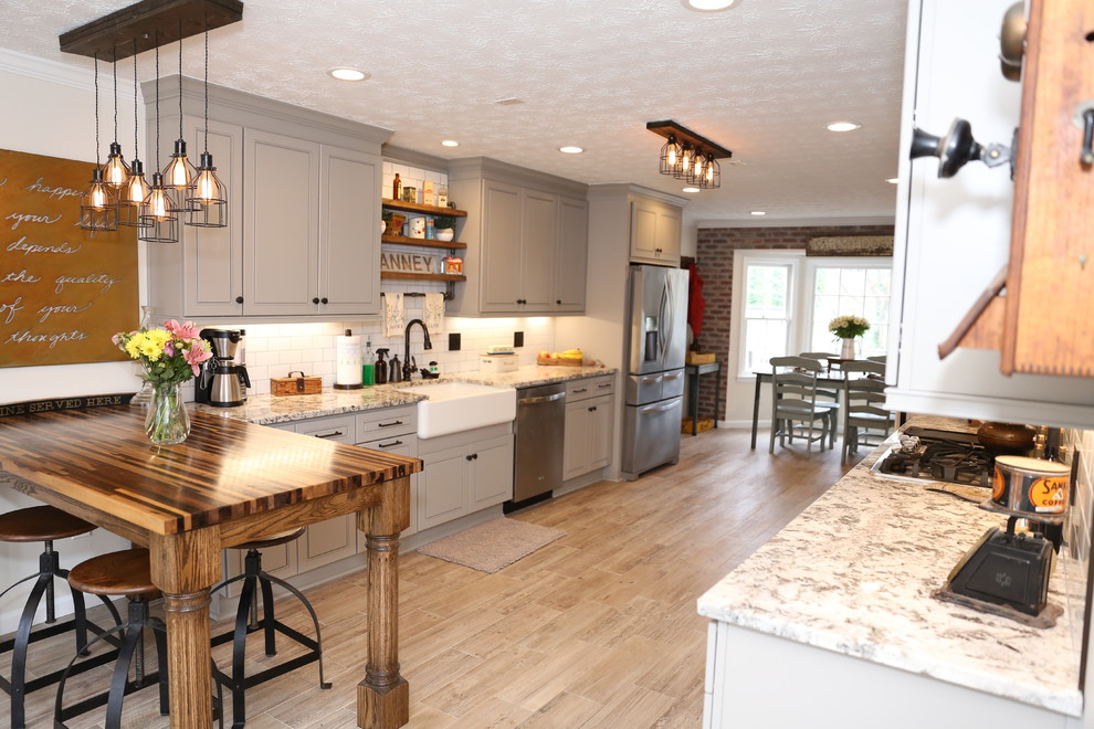 アトランタにある広いカントリー風のおしゃれなキッチン (エプロンフロントシンク、レイズドパネル扉のキャビネット、グレーのキャビネット、白いキッチンパネル、シルバーの調理設備、淡色無垢フローリング、茶色い床) の写真