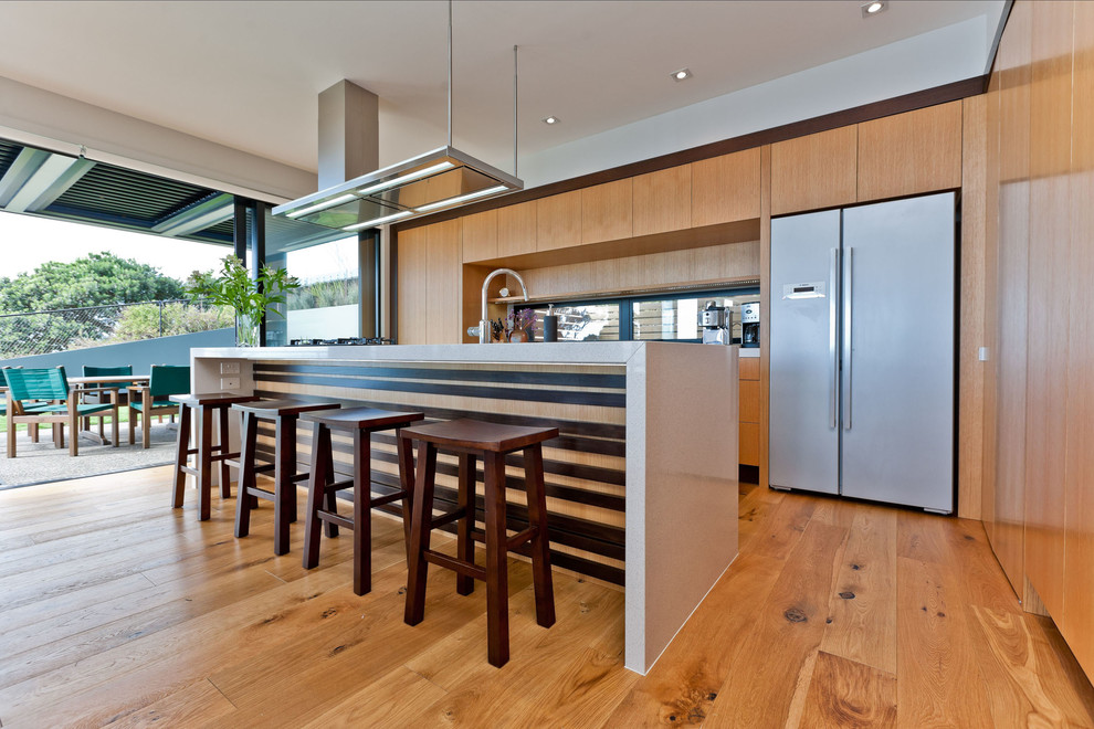 Inspiration for a large contemporary galley kitchen in Auckland with a built-in sink, flat-panel cabinets, medium wood cabinets, engineered stone countertops, stainless steel appliances, light hardwood flooring and an island.