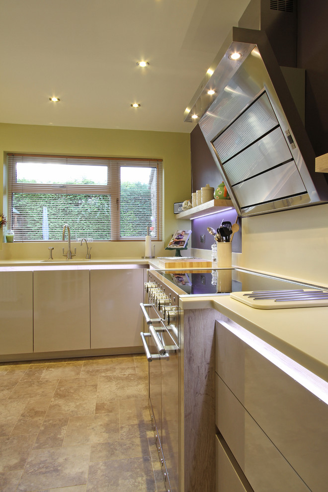 Mid-sized minimalist l-shaped eat-in kitchen photo in Hampshire with a single-bowl sink, flat-panel cabinets, white cabinets, solid surface countertops, white backsplash, colored appliances and a peninsula