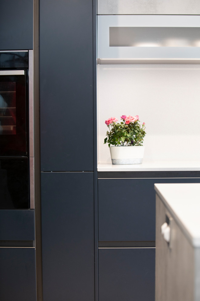 Стильный дизайн: угловая кухня-гостиная среднего размера в современном стиле с накладной мойкой, плоскими фасадами, синими фасадами, столешницей из кварцита, черной техникой, островом и белой столешницей - последний тренд
