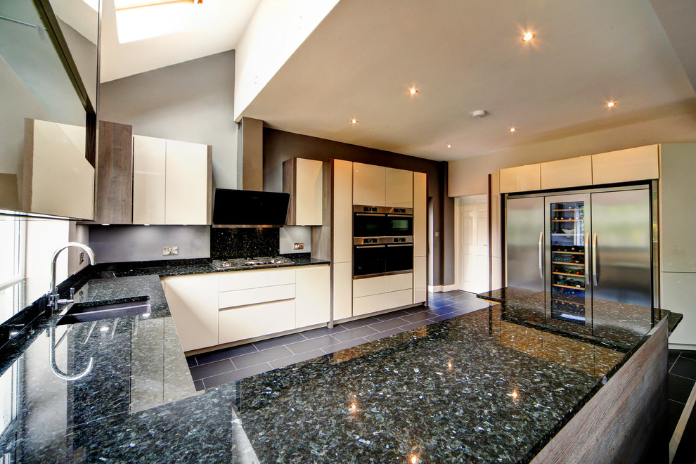 Photo of a large contemporary u-shaped kitchen/diner in Manchester with a built-in sink, flat-panel cabinets, beige cabinets, granite worktops, black splashback, stone slab splashback, stainless steel appliances and porcelain flooring.