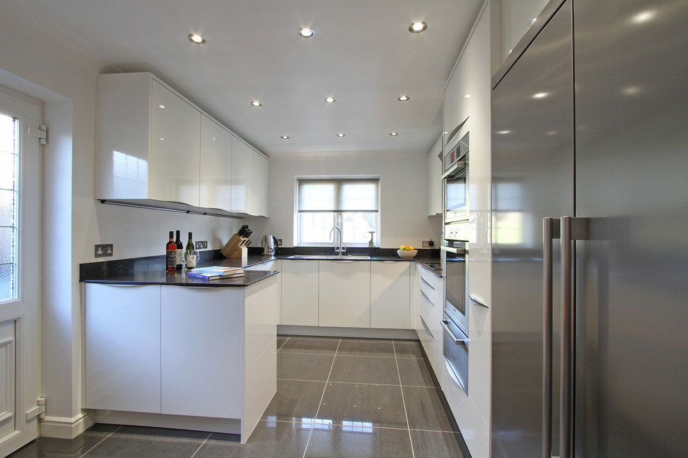 Small contemporary u-shaped enclosed kitchen in Hampshire with a built-in sink, flat-panel cabinets, white cabinets, engineered stone countertops, black splashback, stainless steel appliances, porcelain flooring and a breakfast bar.