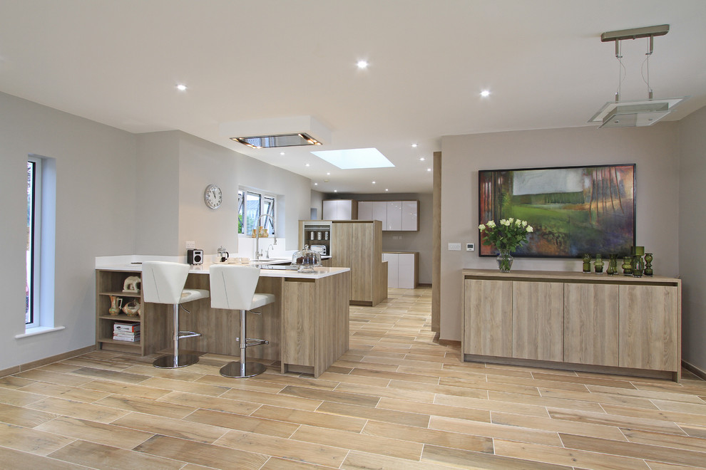 Photo of an expansive contemporary u-shaped open plan kitchen in Hampshire with an integrated sink, flat-panel cabinets, medium wood cabinets, white splashback, stainless steel appliances, ceramic flooring and a breakfast bar.