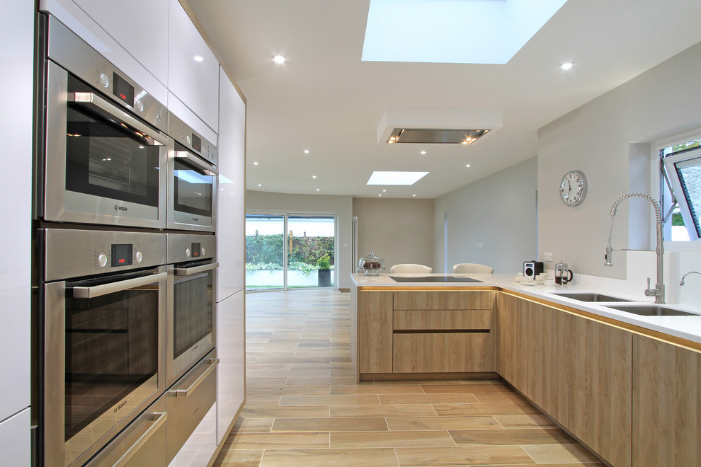 Inspiration for an expansive contemporary u-shaped open plan kitchen in Hampshire with an integrated sink, flat-panel cabinets, medium wood cabinets, white splashback, stainless steel appliances, ceramic flooring and a breakfast bar.
