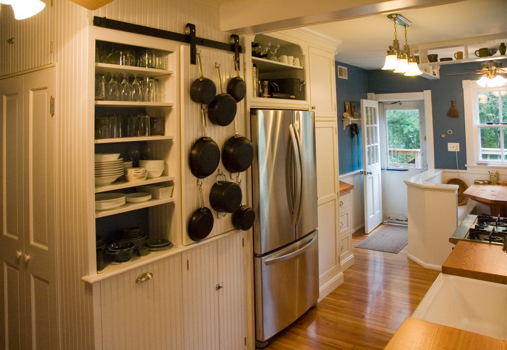 Small country galley kitchen/diner in DC Metro with a belfast sink, beaded cabinets, white cabinets, wood worktops, stainless steel appliances, medium hardwood flooring and no island.