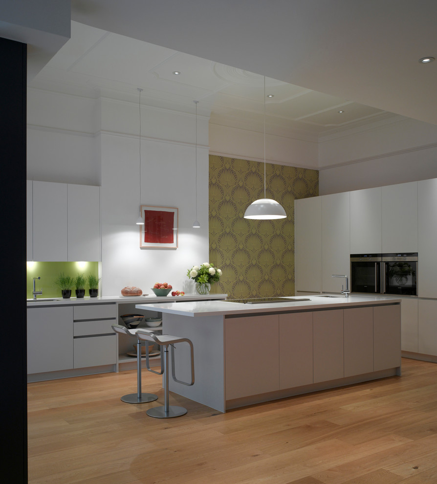 Inspiration for a large contemporary open plan kitchen in London with a submerged sink, flat-panel cabinets, white cabinets, composite countertops, glass sheet splashback, medium hardwood flooring and an island.