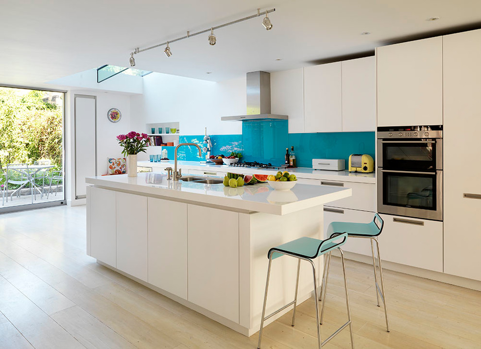 Große Moderne Küche mit flächenbündigen Schrankfronten, Küchenrückwand in Blau, Glasrückwand, hellem Holzboden und Kücheninsel in London