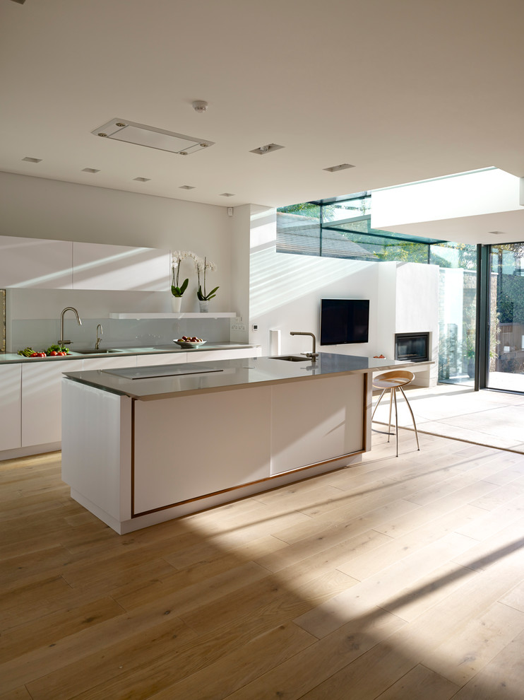 Пример оригинального дизайна: кухня-гостиная в современном стиле с плоскими фасадами, белыми фасадами, светлым паркетным полом и островом