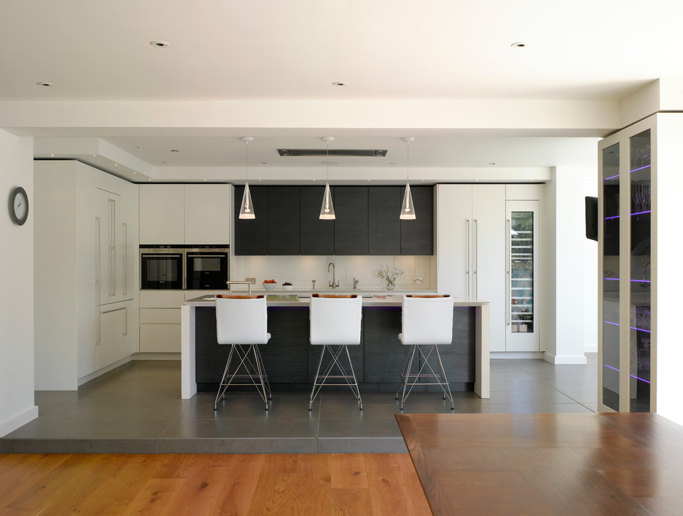 Large open concept kitchen photo in London with flat-panel cabinets, solid surface countertops, white backsplash and an island