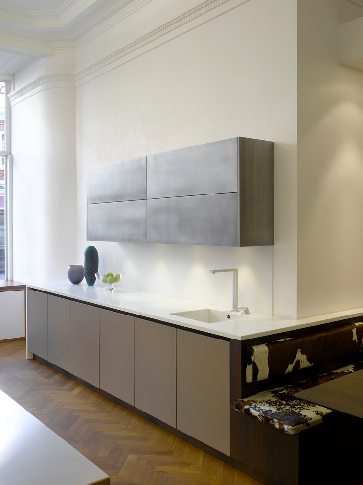 Cette image montre une grande cuisine ouverte design avec un évier intégré, un placard à porte plane, un plan de travail en surface solide et une crédence blanche.