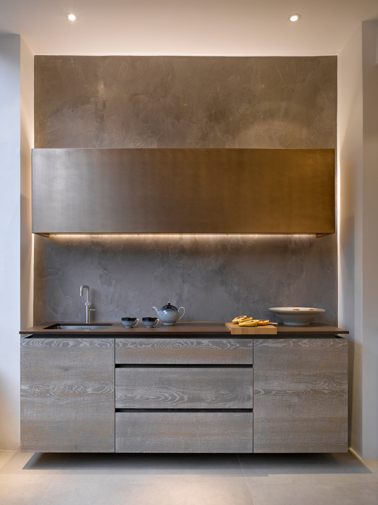 Exemple d'une grande cuisine ouverte tendance en bois vieilli avec un placard à porte plane, un plan de travail en surface solide, une crédence grise et un évier encastré.