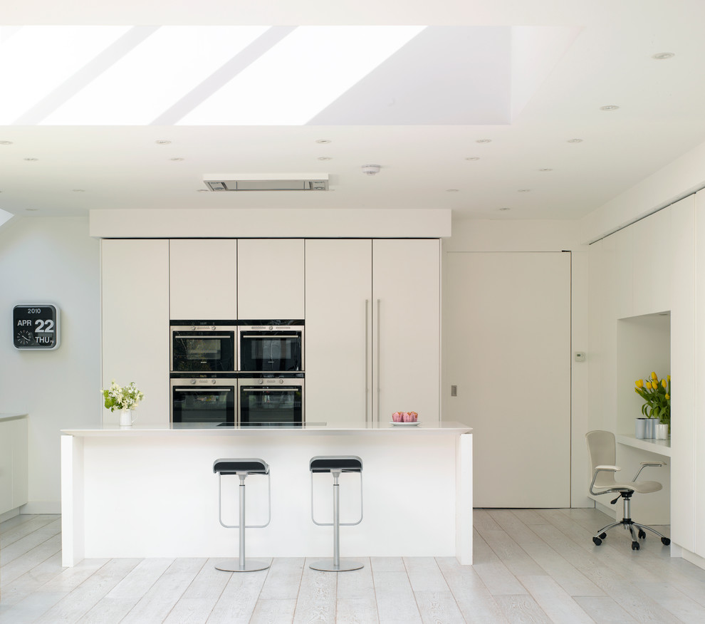 This is an example of a large scandi open plan kitchen in London with flat-panel cabinets, white cabinets, composite countertops and an island.