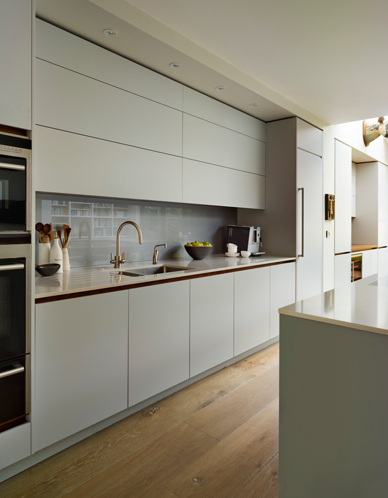 Design ideas for a large contemporary open plan kitchen in London with a submerged sink, flat-panel cabinets, blue cabinets, composite countertops, grey splashback, glass sheet splashback and an island.