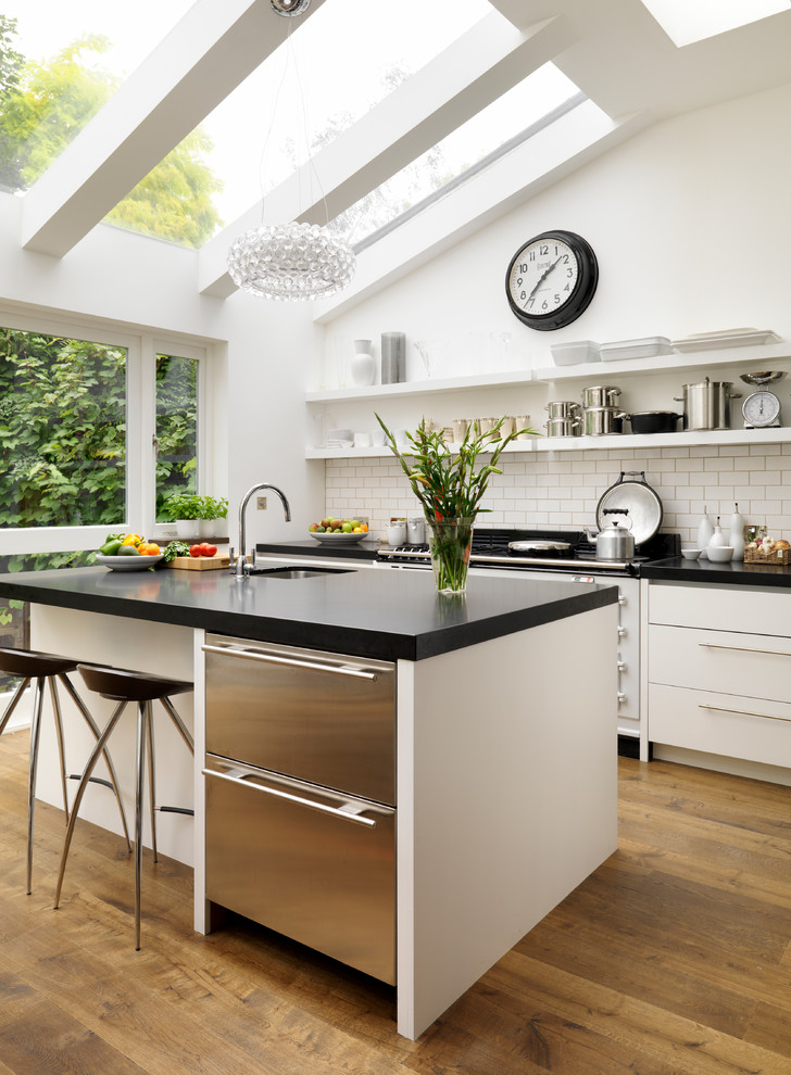 Large trendy kitchen photo in London with flat-panel cabinets, white cabinets, solid surface countertops and an undermount sink