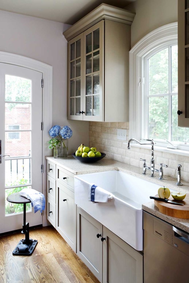 ワシントンD.C.にあるトラディショナルスタイルのおしゃれなII型キッチン (エプロンフロントシンク、ガラス扉のキャビネット、ライムストーンのキッチンパネル、グレーとクリーム色) の写真