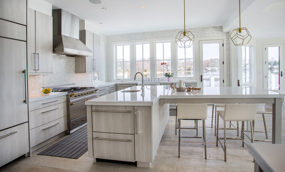 Example of a large trendy l-shaped medium tone wood floor open concept kitchen design in New York with a farmhouse sink, flat-panel cabinets, gray cabinets, glass countertops, gray backsplash, stone tile backsplash, stainless steel appliances and an island
