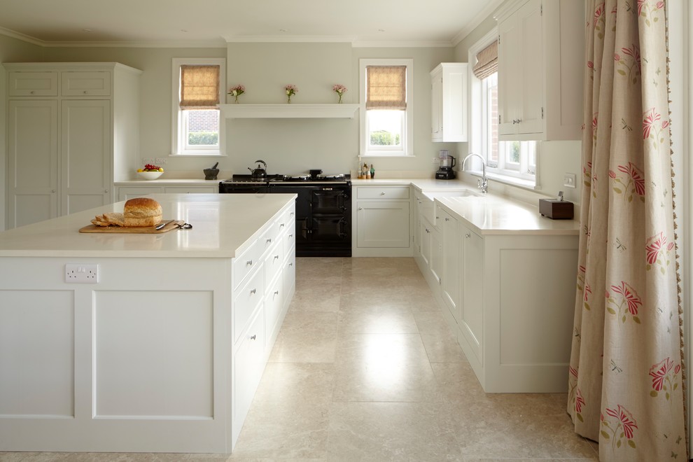 Design ideas for a medium sized classic l-shaped open plan kitchen in Hampshire with a belfast sink, shaker cabinets, white cabinets, quartz worktops, black appliances, limestone flooring, an island, beige floors and white worktops.