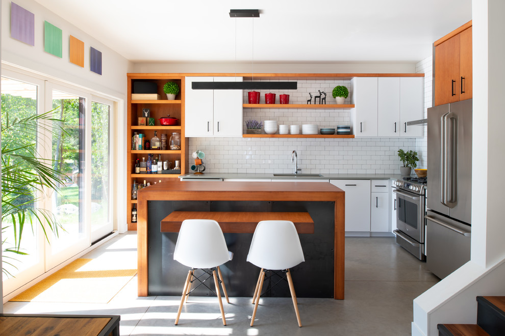 Inredning av ett modernt grå grått l-kök, med en enkel diskho, öppna hyllor, skåp i mellenmörkt trä, vitt stänkskydd, stänkskydd i tunnelbanekakel, rostfria vitvaror, betonggolv, en köksö och grått golv