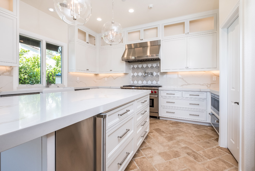 Medium sized traditional l-shaped enclosed kitchen in Orange County with recessed-panel cabinets, white cabinets, engineered stone countertops, white splashback, marble splashback, stainless steel appliances, porcelain flooring, an island, beige floors and a belfast sink.