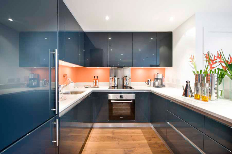 Modern inredning av ett mellanstort kök, med en undermonterad diskho, släta luckor, blå skåp, bänkskiva i kvarts, orange stänkskydd, glaspanel som stänkskydd och rostfria vitvaror