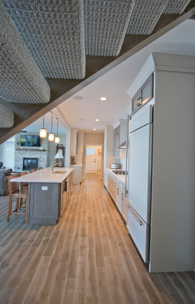 Elegant galley medium tone wood floor and brown floor open concept kitchen photo in Other with an undermount sink, recessed-panel cabinets, quartz countertops, beige backsplash, mosaic tile backsplash, paneled appliances, an island, white countertops and beige cabinets