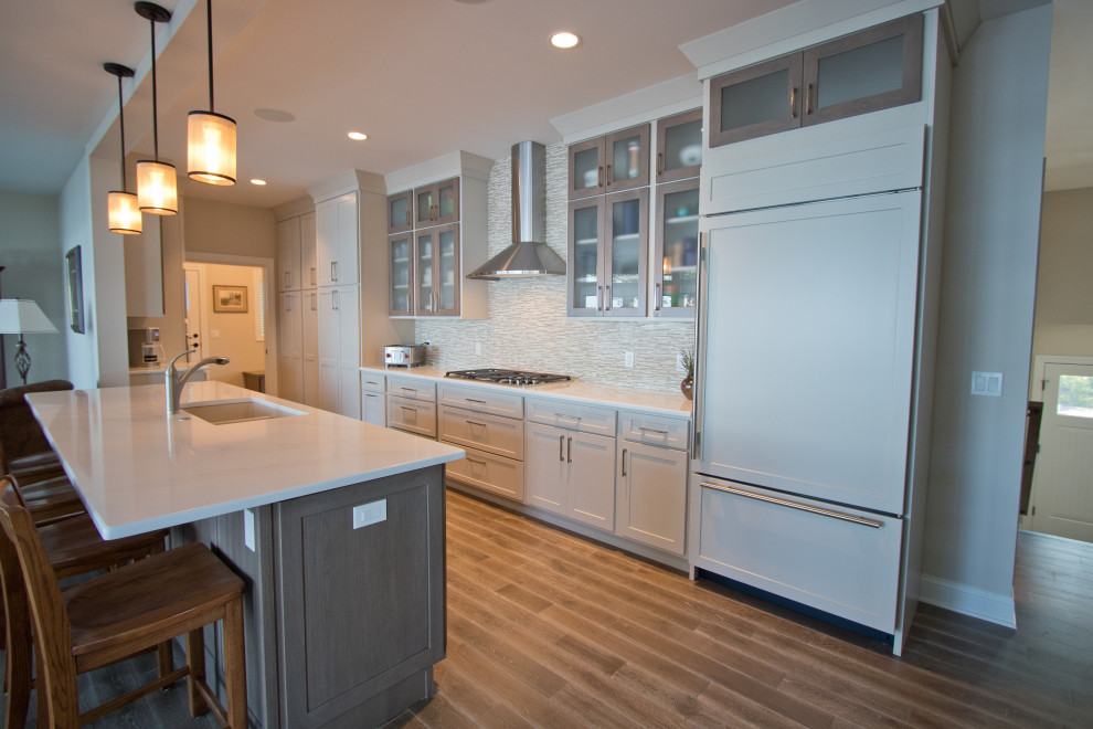 Example of a classic galley medium tone wood floor and brown floor open concept kitchen design in Other with an undermount sink, recessed-panel cabinets, quartz countertops, beige backsplash, mosaic tile backsplash, paneled appliances, an island, white countertops and beige cabinets