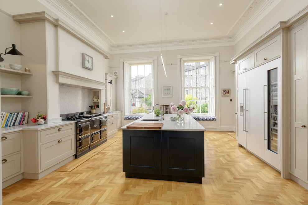 Modern inredning av ett stort grå grått kök, med en integrerad diskho, skåp i shakerstil, blå skåp, bänkskiva i kvarts, integrerade vitvaror, ljust trägolv, en köksö och brunt golv