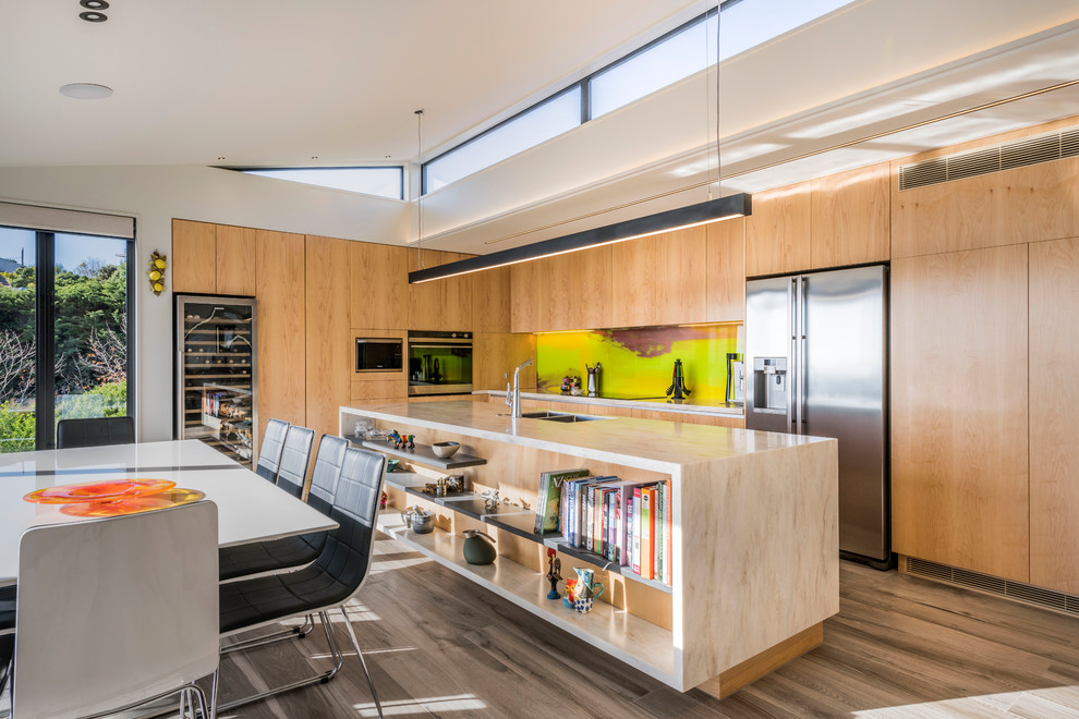 World-inspired l-shaped open plan kitchen in Christchurch with a submerged sink, flat-panel cabinets, light wood cabinets, multi-coloured splashback, stainless steel appliances, an island, grey floors and beige worktops.