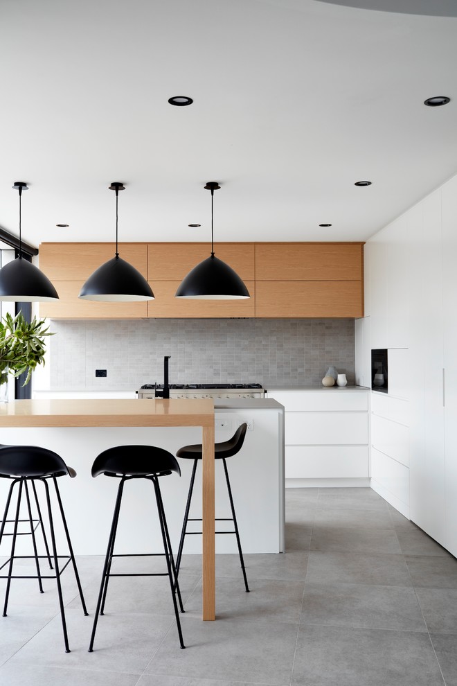 На фото: параллельная кухня в стиле модернизм с плоскими фасадами, светлыми деревянными фасадами, серым фартуком, островом, серым полом и серой столешницей с