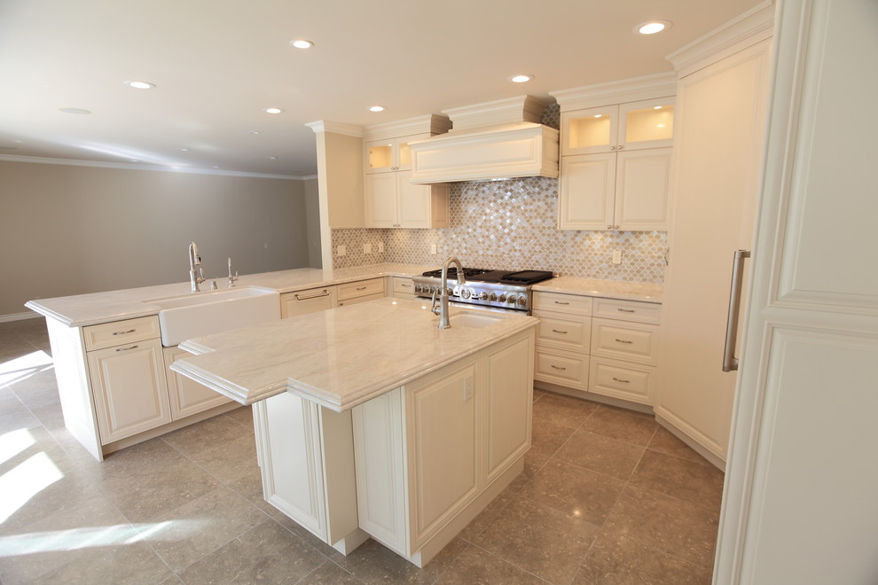 Example of a mid-sized classic u-shaped slate floor eat-in kitchen design in Los Angeles with a farmhouse sink, raised-panel cabinets, beige cabinets, limestone countertops, beige backsplash, glass tile backsplash, colored appliances and an island