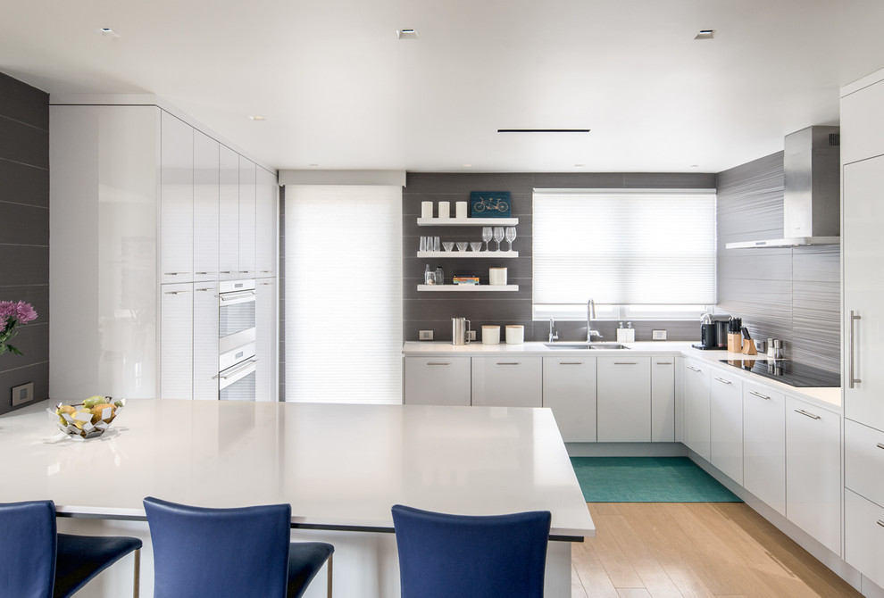 Example of a mid-sized minimalist l-shaped light wood floor and brown floor enclosed kitchen design in Denver with flat-panel cabinets, white cabinets, paneled appliances, an island, a double-bowl sink, solid surface countertops, gray backsplash and stone slab backsplash